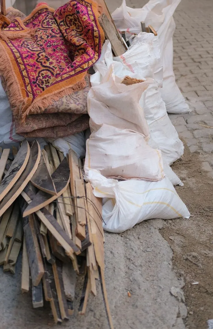 Old rugs, cut timber and sacks of waste stacked against a wall ready for the skip