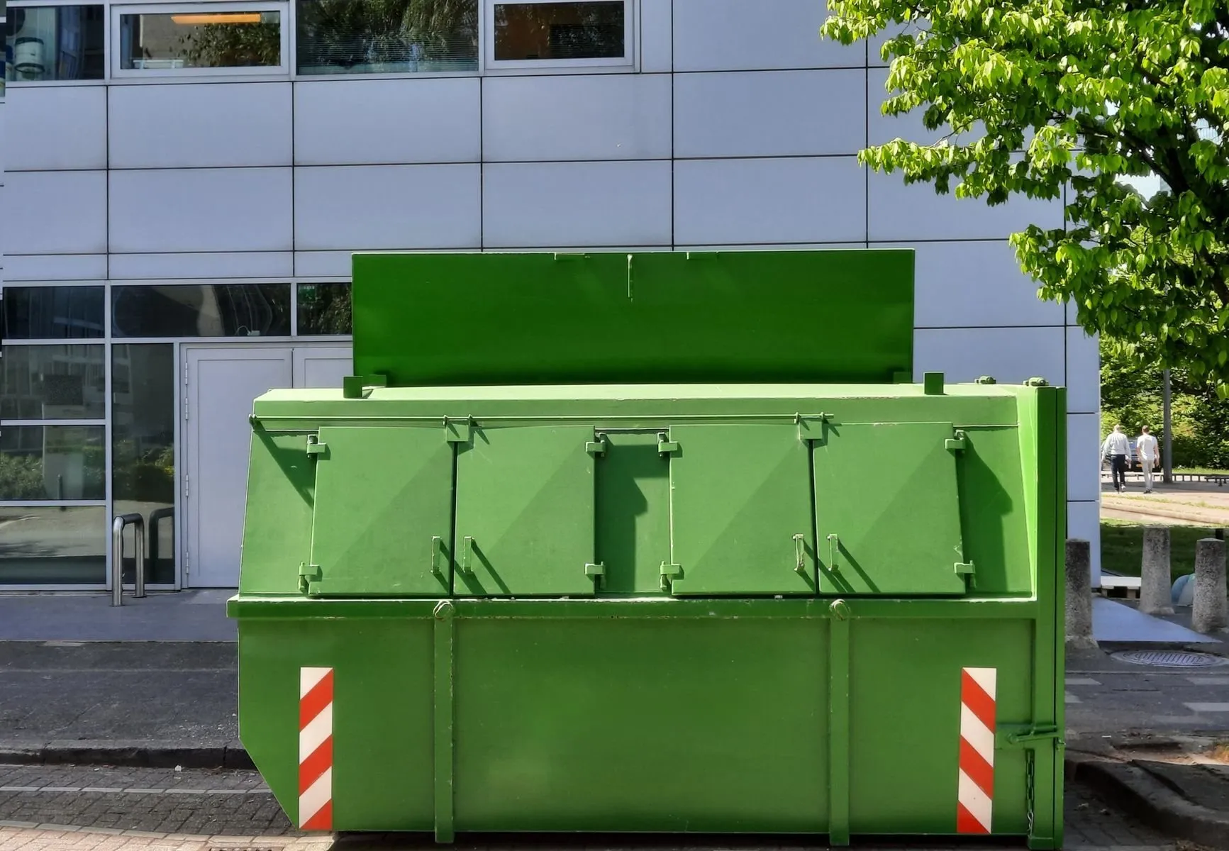 A green enclosed skip with hinged steel lids standing outside an office building