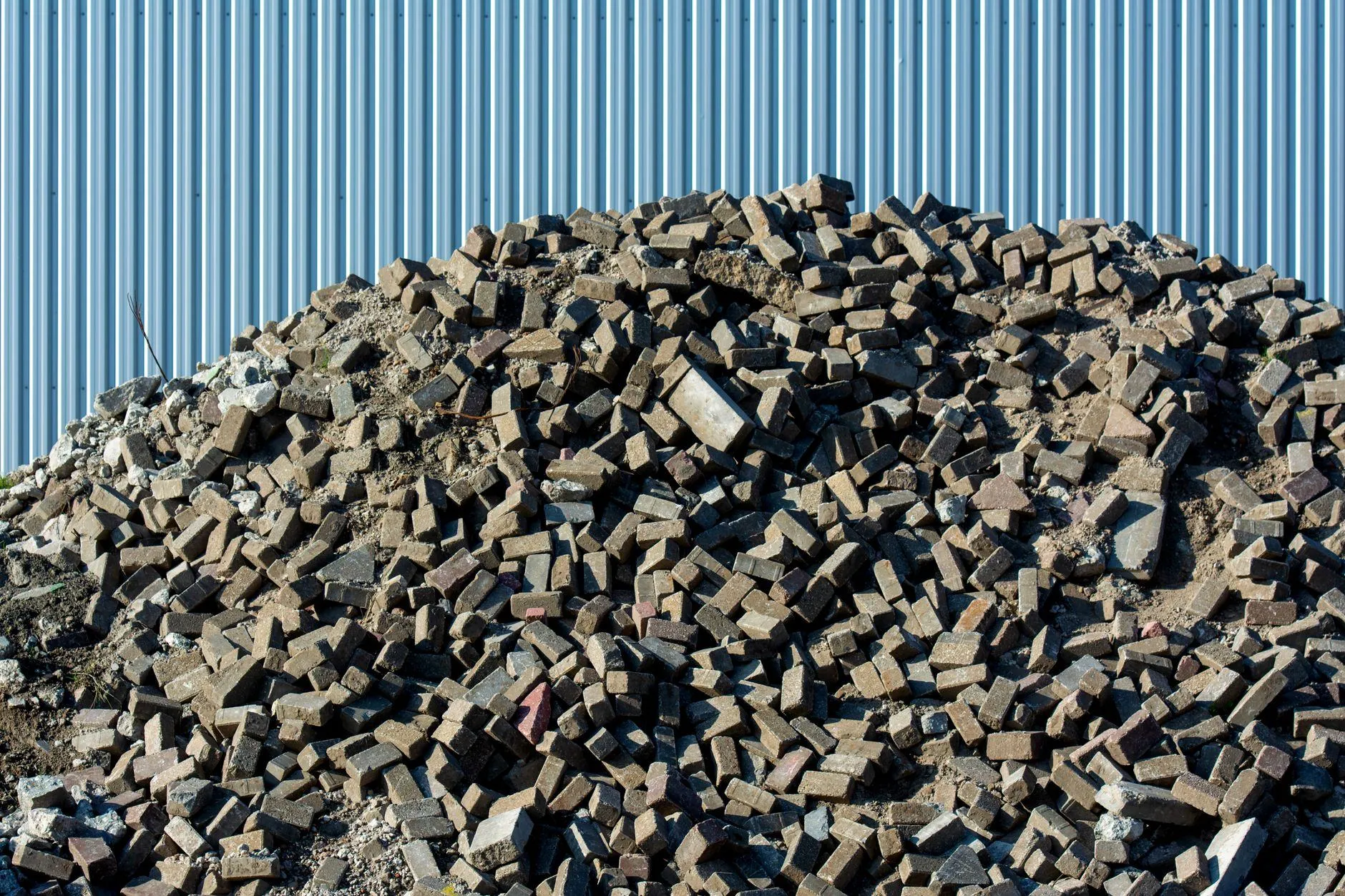 A heap of broken brick pavers and rubble against a pale corrugated metal wall