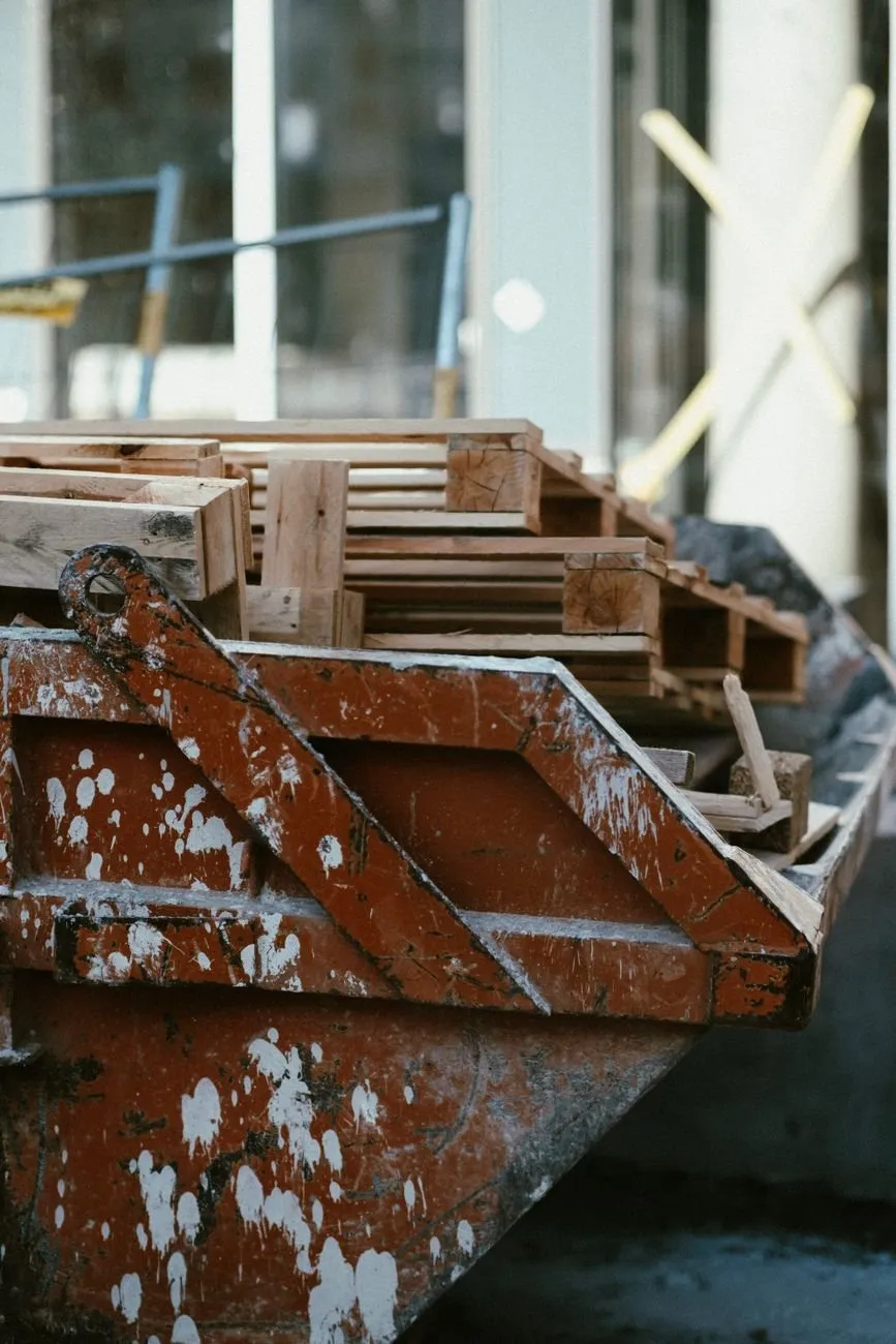 A paint-spattered builders’ skip loaded with broken timber pallets outside a building site